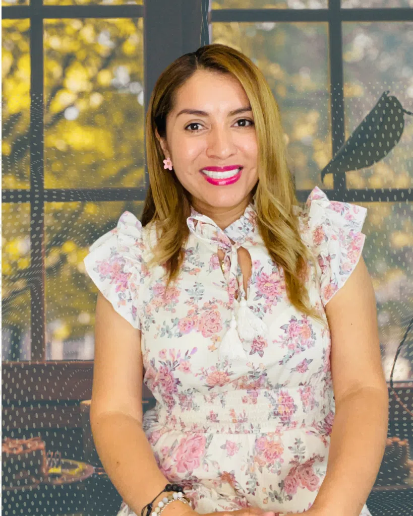 Mujer sonriente con vestido floral delante de ventana.