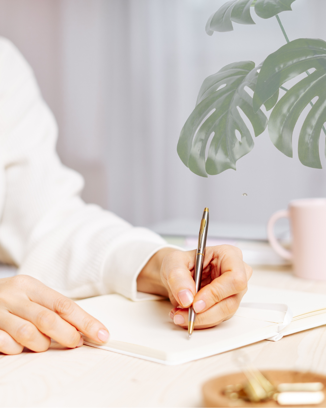 Manos escribiendo en cuaderno con bolígrafo plateado.